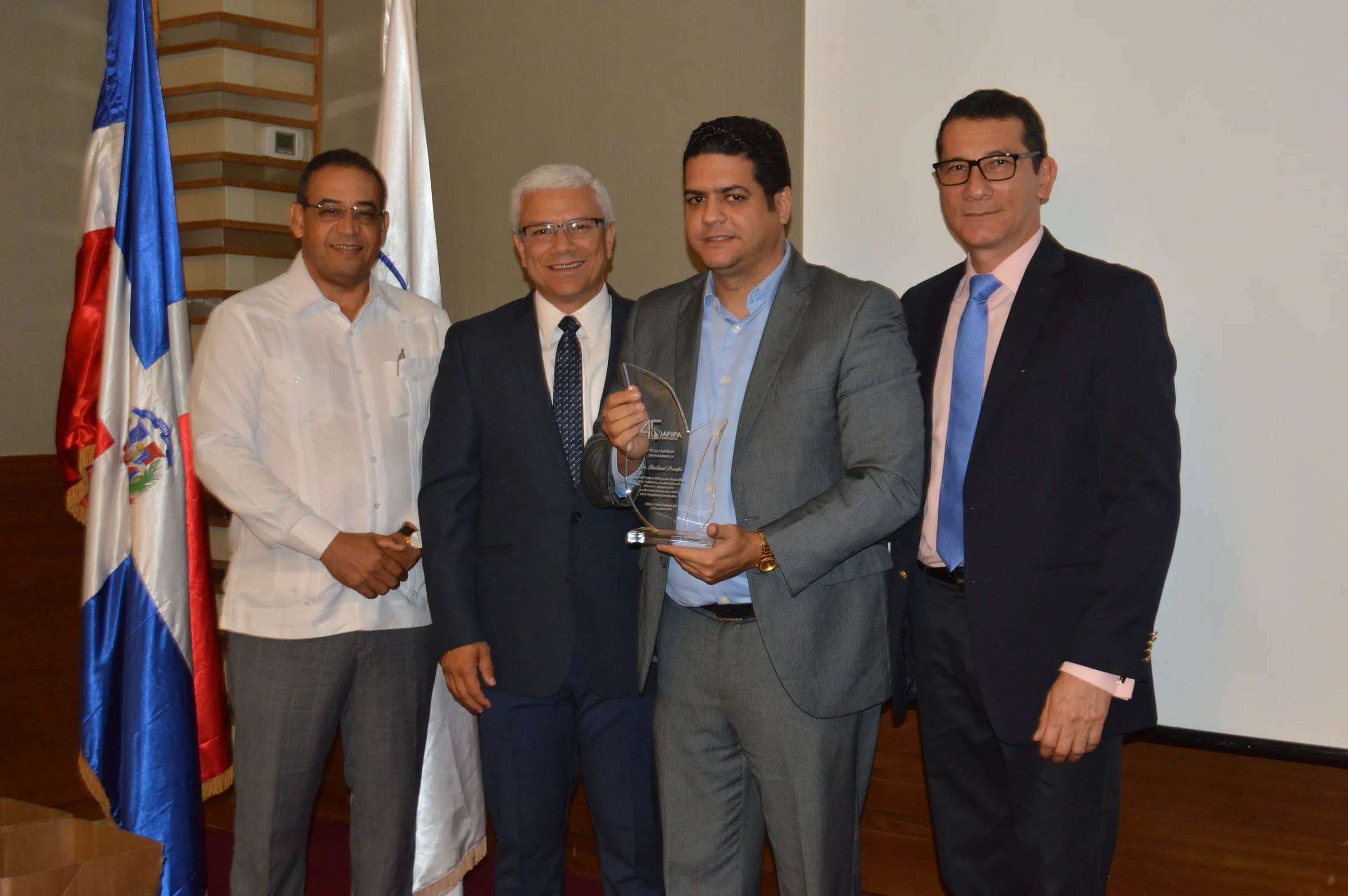 Un colaborador de AFIPA sostiene la placa que acaba de recibir, entre tres directivos de la asociación