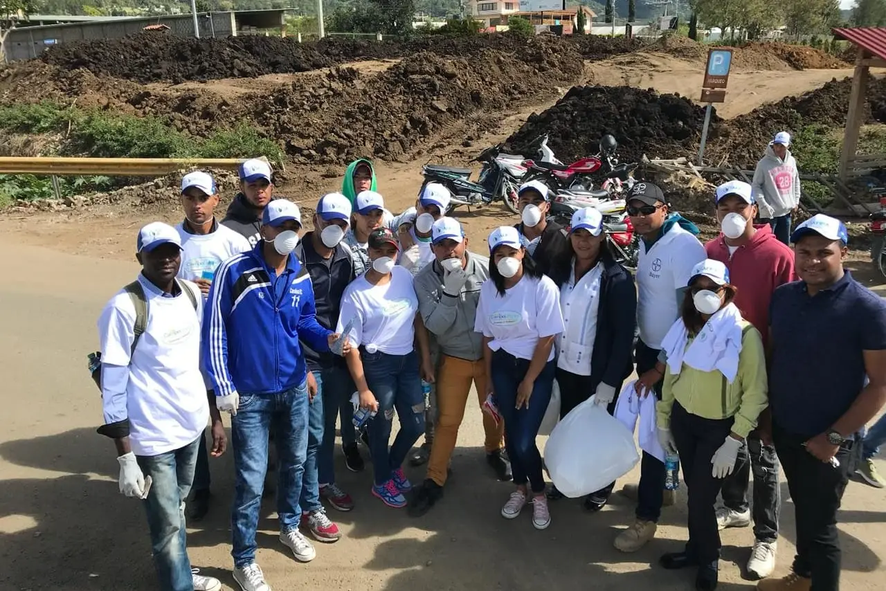 Grupo de voluntarios con camisetas blancas, gorras y guantes posa en un camino de tierra de Tireo antes de empezar la recolección