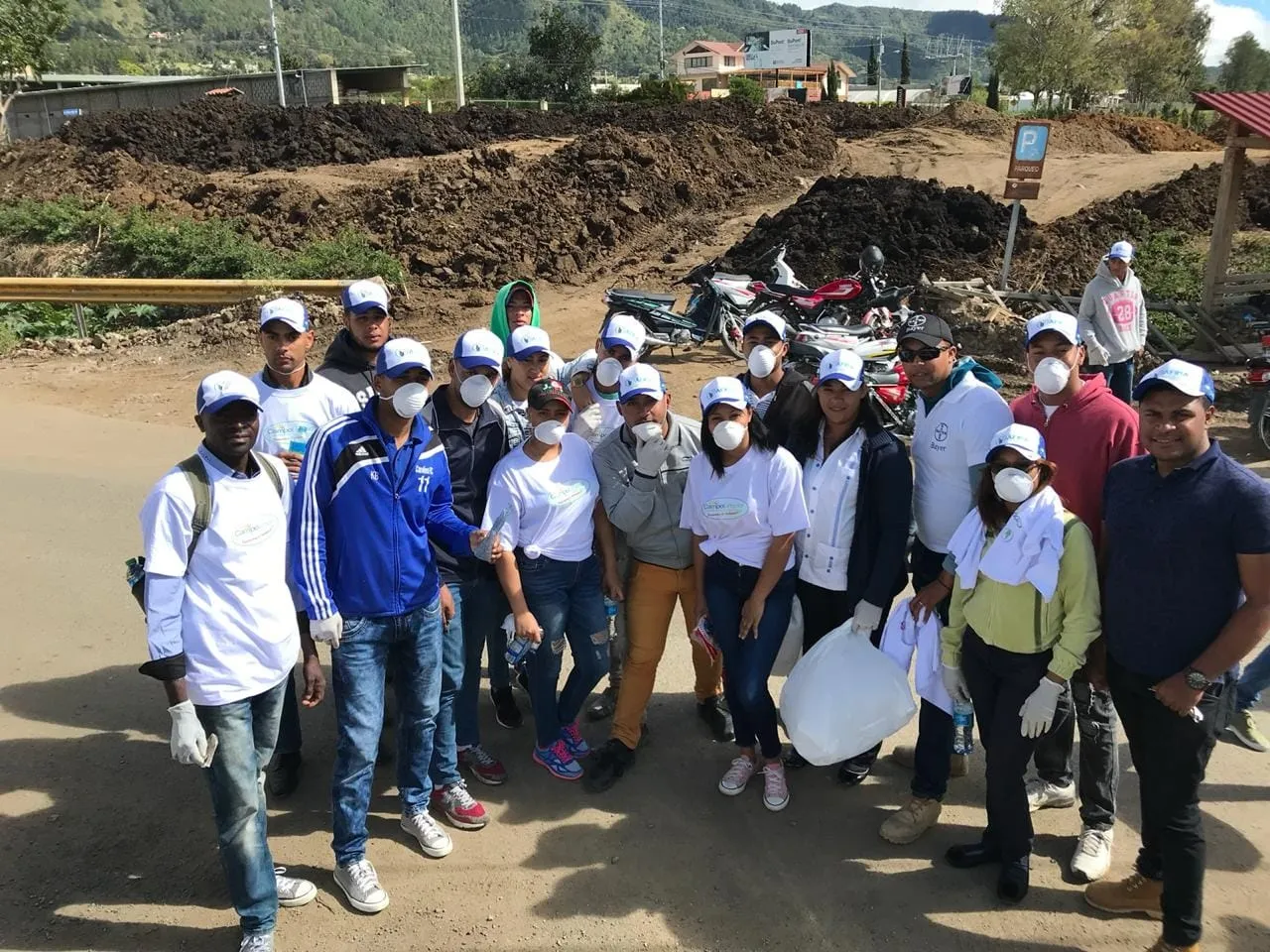 Grupo de voluntarios con camisetas blancas, gorras y guantes posa en un camino de tierra de Tireo antes de empezar la recolección
