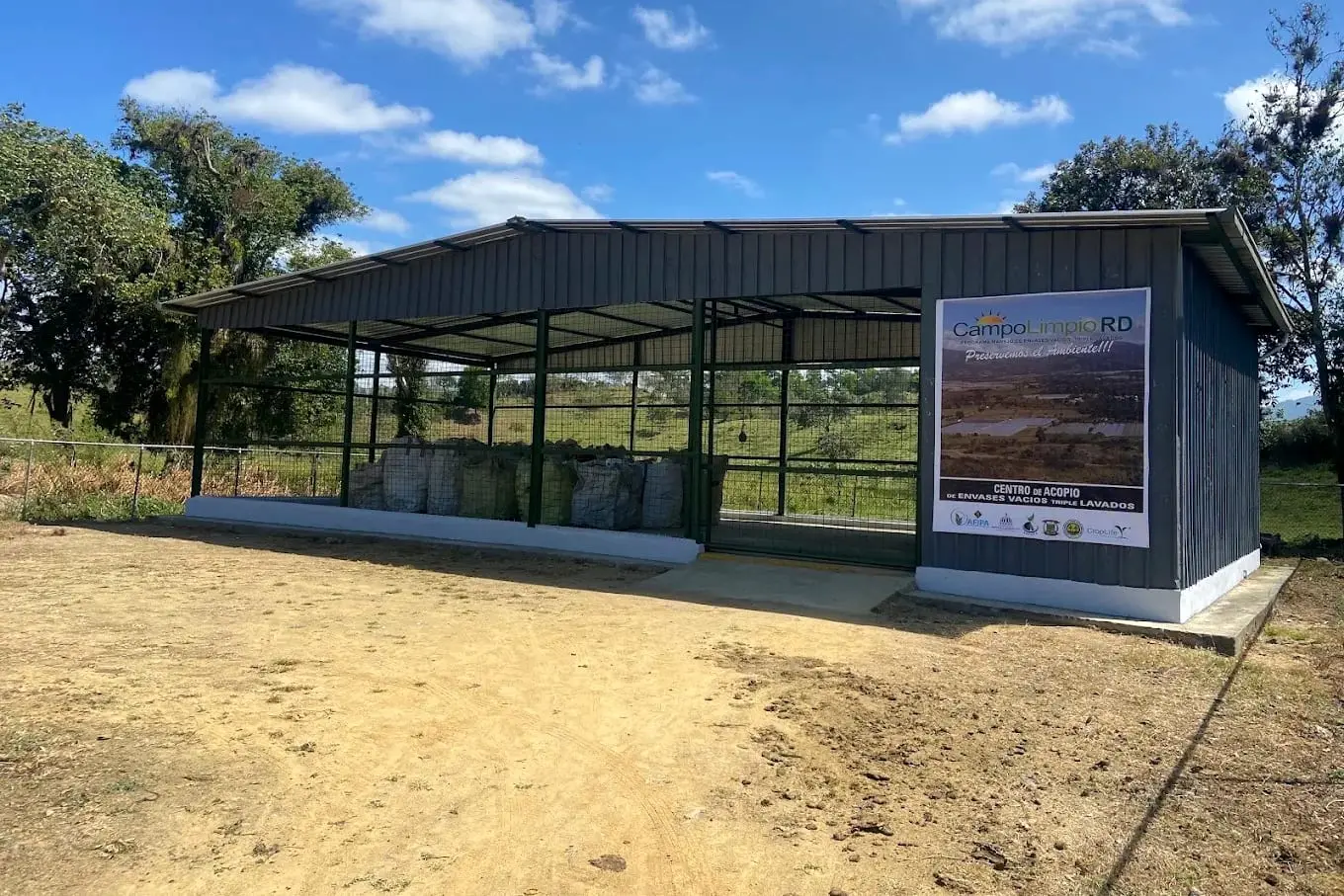 Galpón de malla del centro de acopio de Rancho Arriba, con sacos de envases vacíos dentro y un letrero de Campo Limpio RD en la fachada