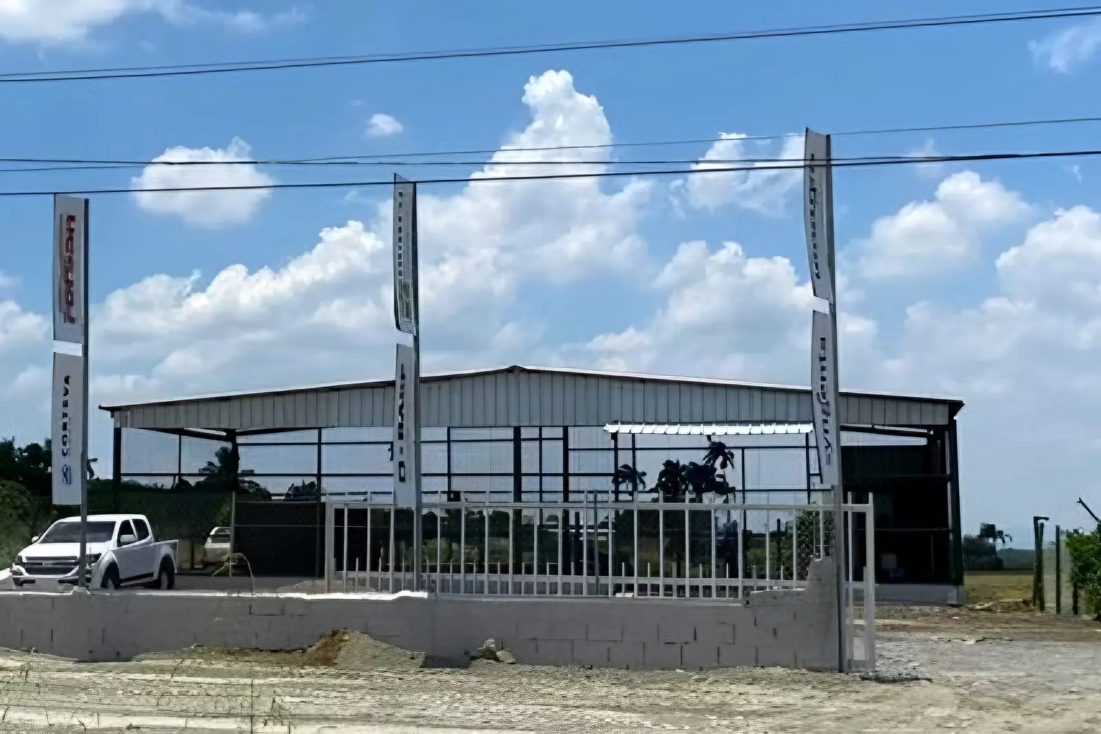 Nave techada del centro de acopio de Rincón, detrás de un muro bajo y una verja, con banderolas de empresas del sector al frente
