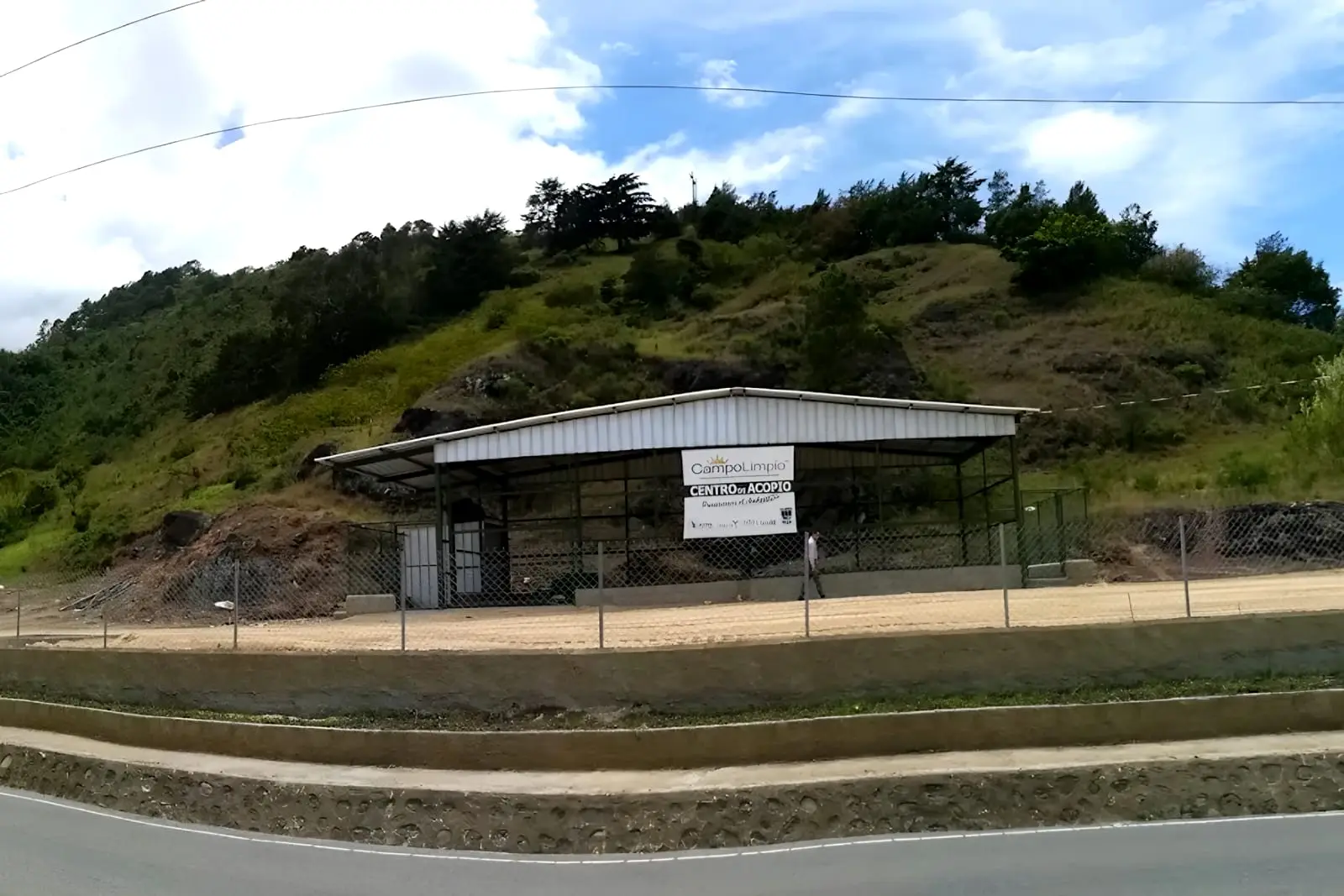 Nave techada del centro de acopio de Tireo, junto a la carretera y al pie de una loma sembrada